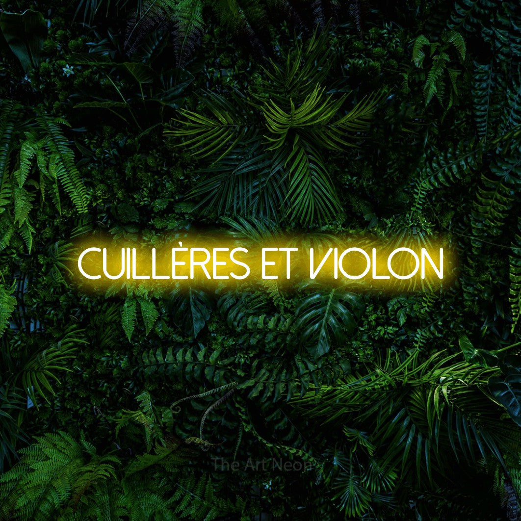 “Cuillères et violon” LED neon sign in yellow, with thin sans-serif lettering, shown against dense tropical foliage.