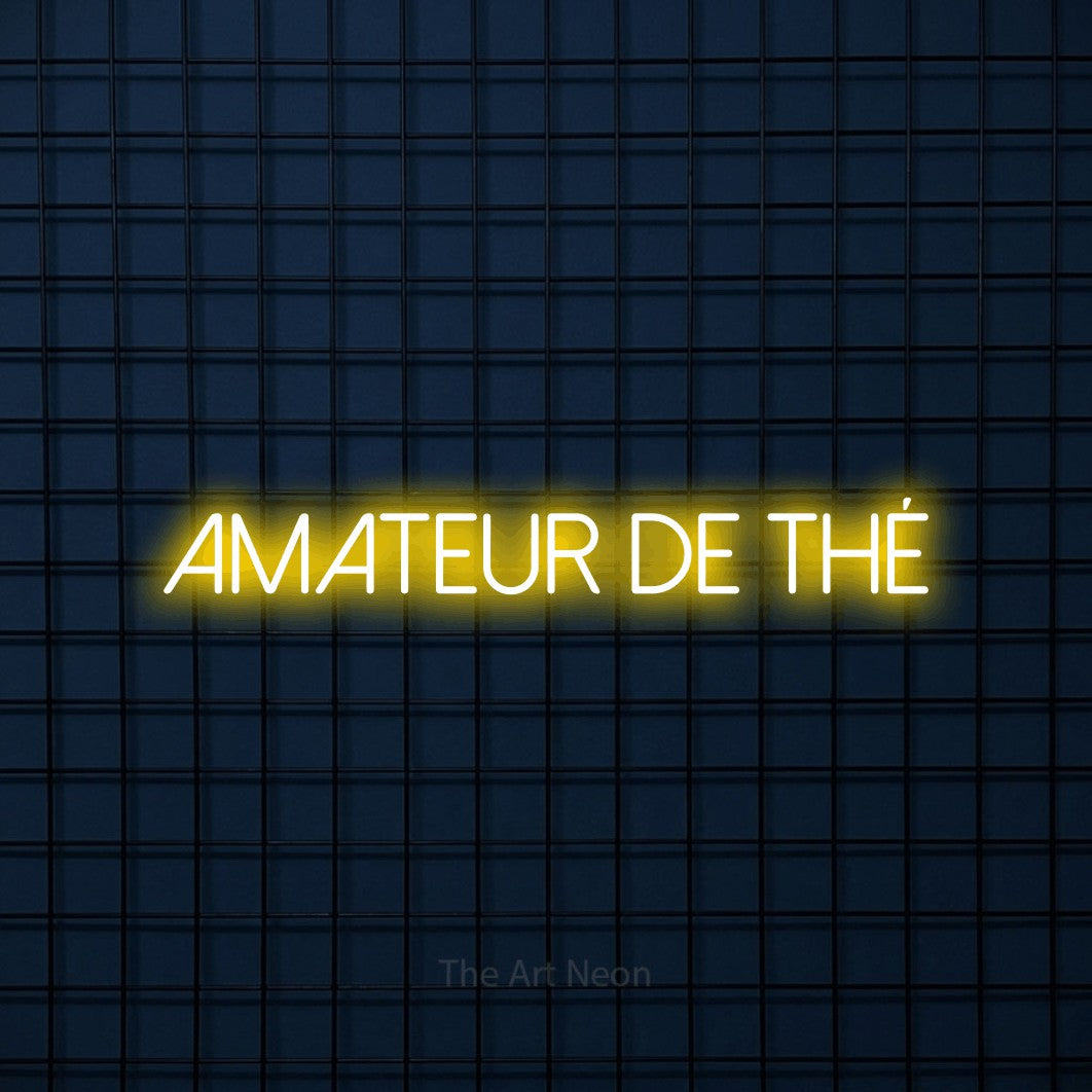 “Amateur de thé” LED neon sign in yellow, with thin sans-serif lettering, shown against a dark blue grid.