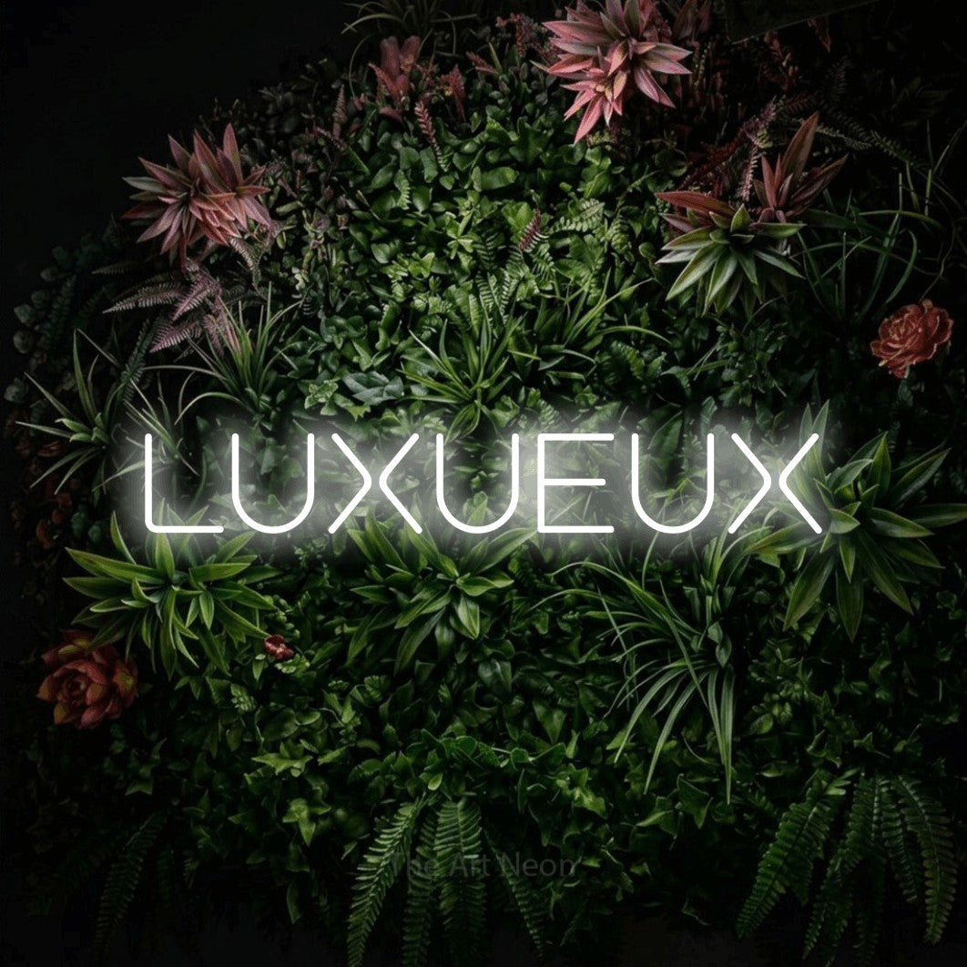 Composition en néon LED « Luxueux » en blanc froid, en lettres géométriques stylisées, mise en valeur sur un mur végétal fleuri, pour une boutique ou un commerce.