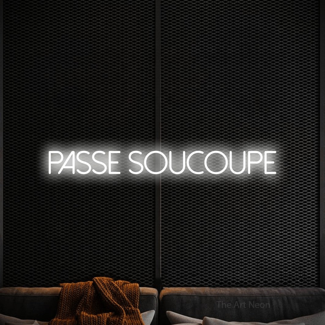 Composition en néon LED « Passe soucoupe » en blanc froid, en lettres fines sans empattement, mise en valeur dans un coin salon moderne aux tons noirs, pour un décor de hockey.