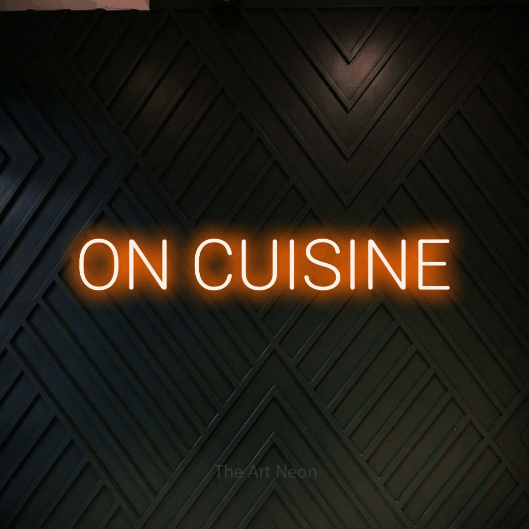 “On cuisine” LED neon sign in orange, with rounded sans-serif lettering, shown against a black chevron-patterned wood wall.