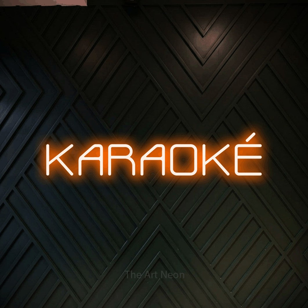 “Karaoké” LED neon sign in orange, with rounded geometric lettering, shown against a black chevron-patterned wood wall.