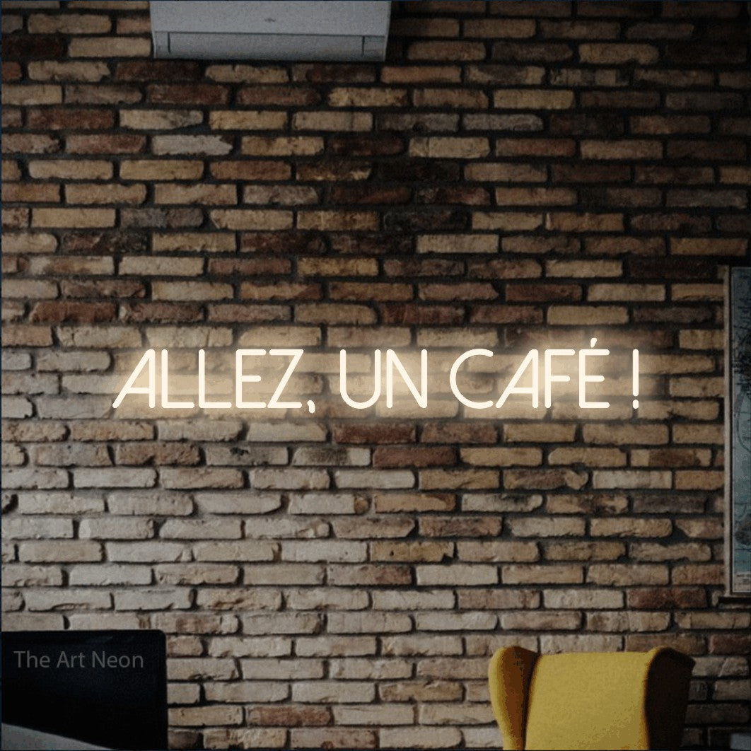 “Allez, un café !” LED neon sign in warm white, with thin sans-serif lettering, shown against warm-toned brickwork.
