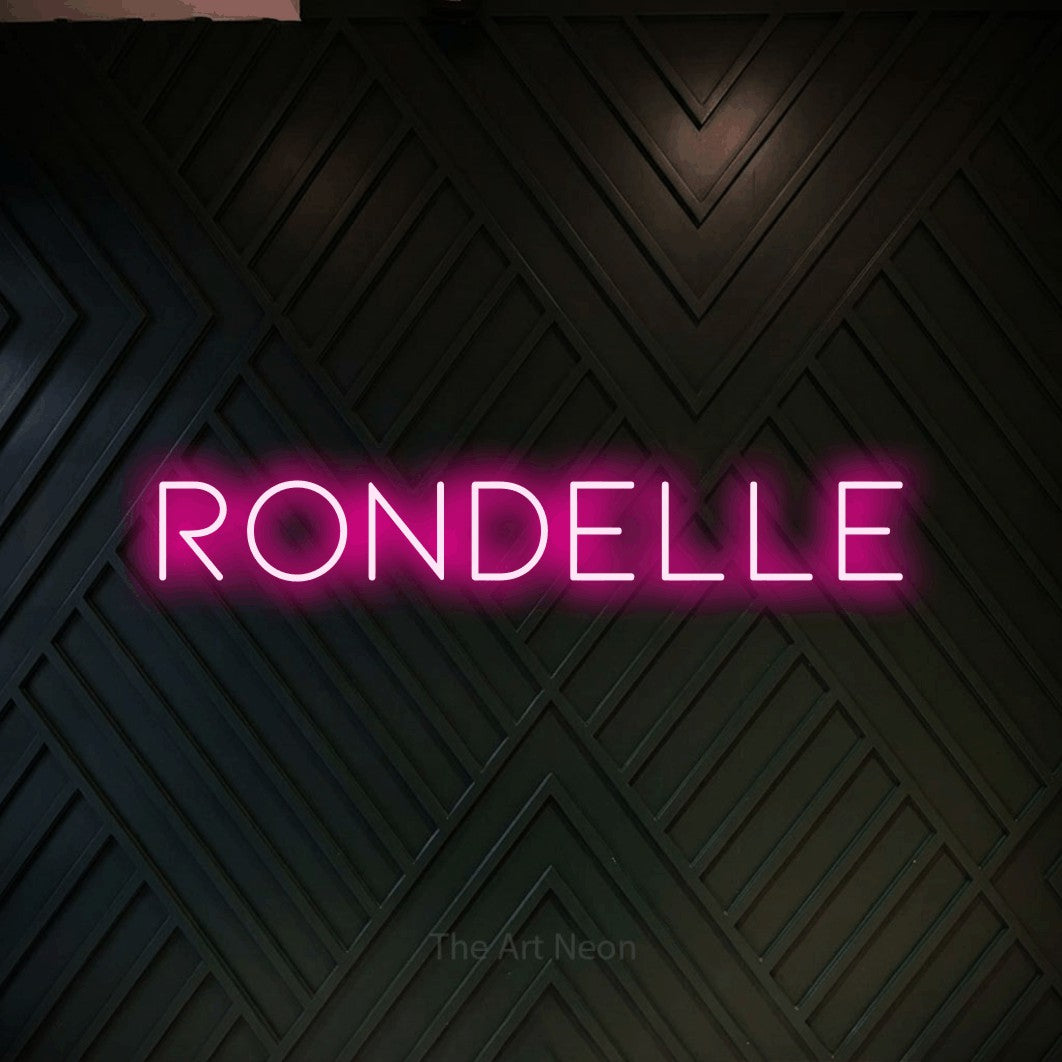 “Rondelle” LED neon sign in hot pink, with thin, widely spaced lettering, shown against a black chevron-patterned wood wall.