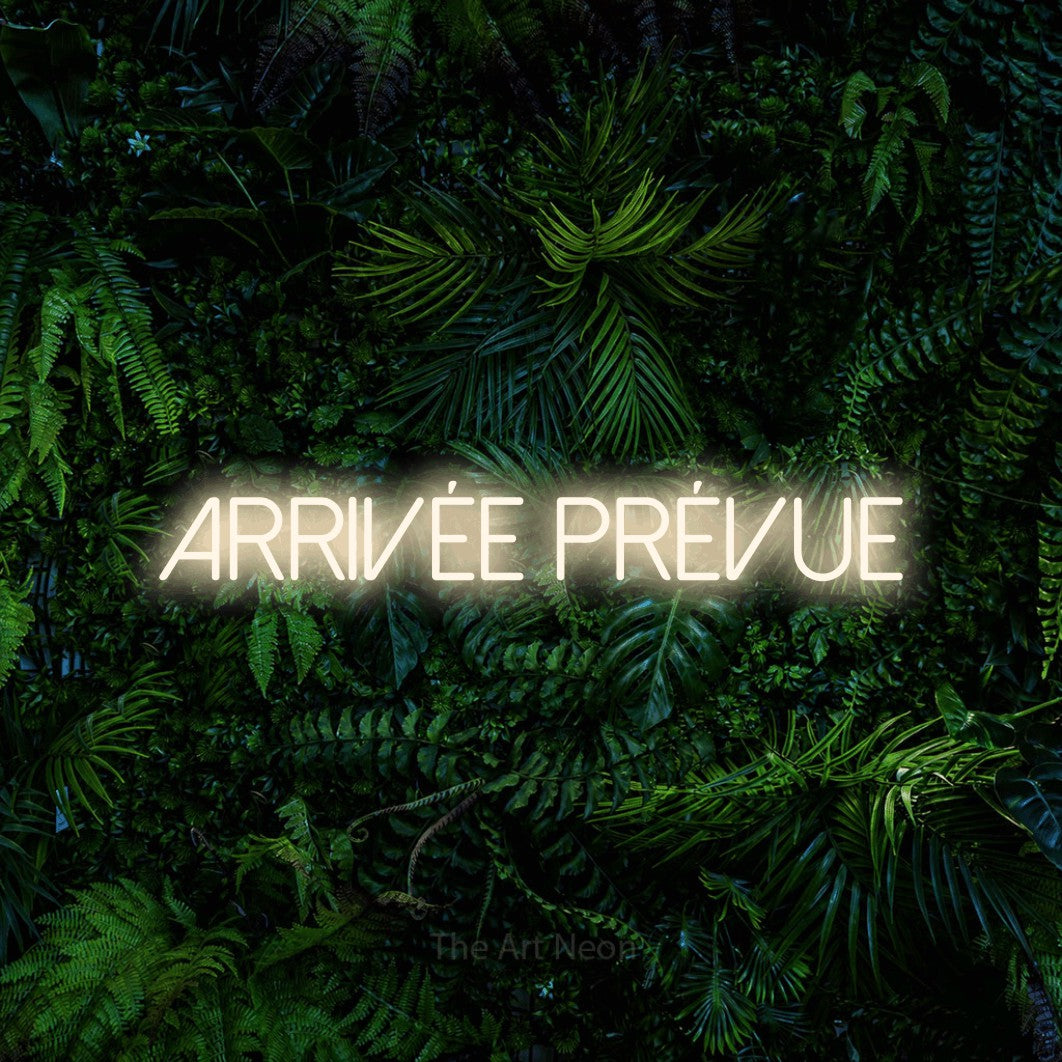 Composition en néon LED « Arrivée prévue » en blanc chaud, en lettres fines sans empattement, mise en valeur devant un feuillage tropical dense, pour une fête prénatale.