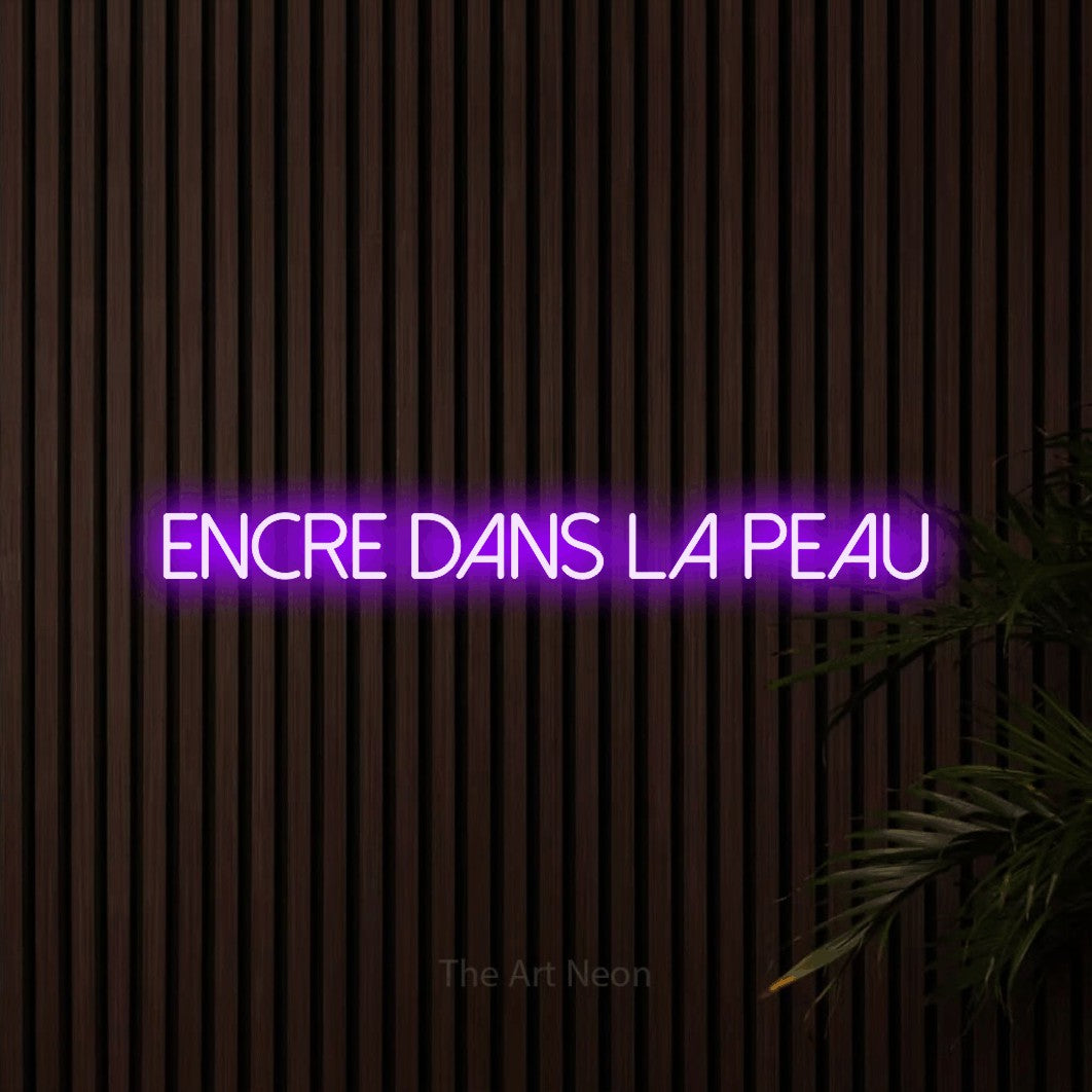 “Encre dans la peau” LED neon sign in purple, with thin sans-serif lettering, shown against dark wooden wall slats.