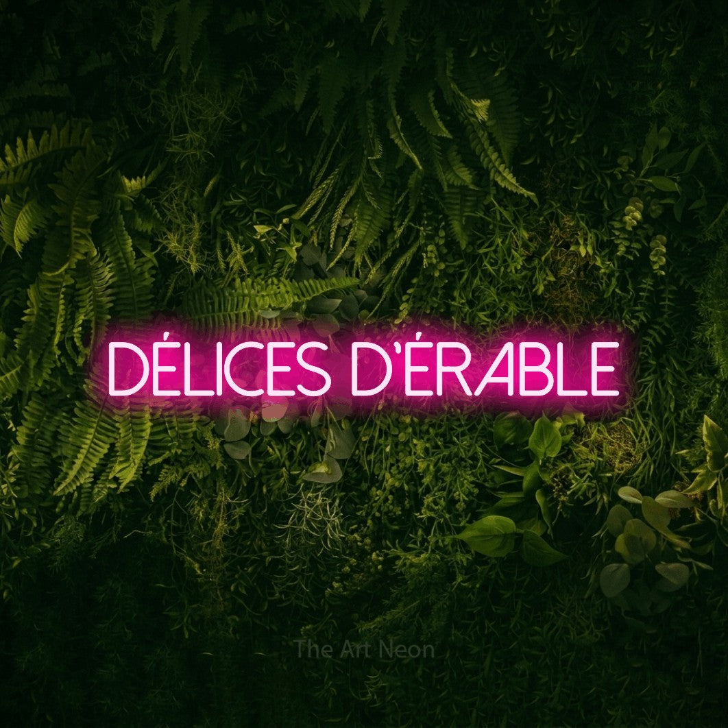 “Délices d'érable” LED neon sign in hot pink, with thin sans-serif lettering, shown against a dark moss and forest backdrop.