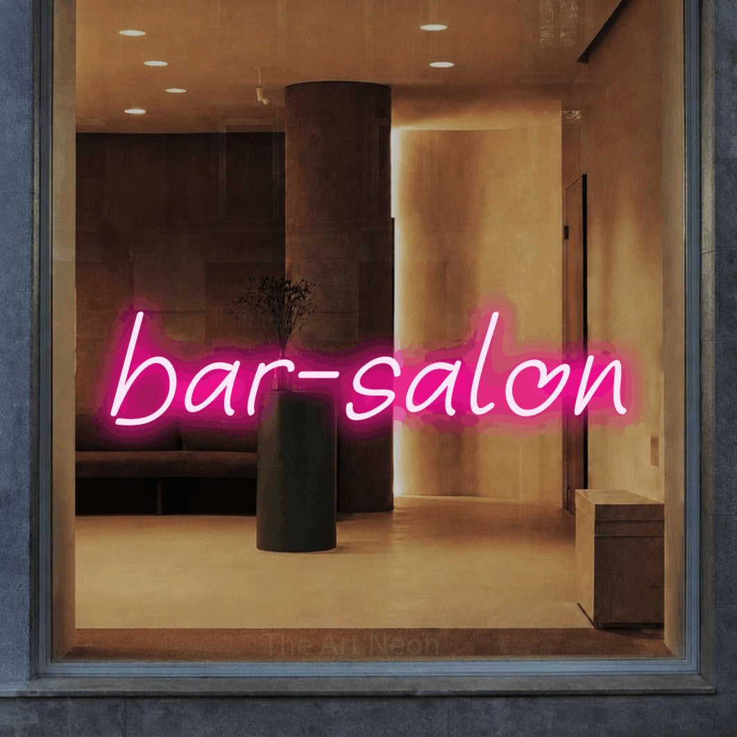 “Bar-salon” LED neon sign in hot pink, with slanted handwritten lettering, shown against a warm-toned interior.