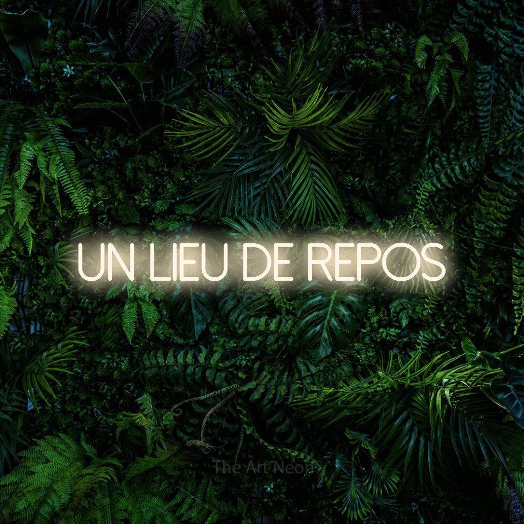 “Un lieu de repos” LED neon sign in warm white, with thin sans-serif lettering, shown against dense tropical foliage.