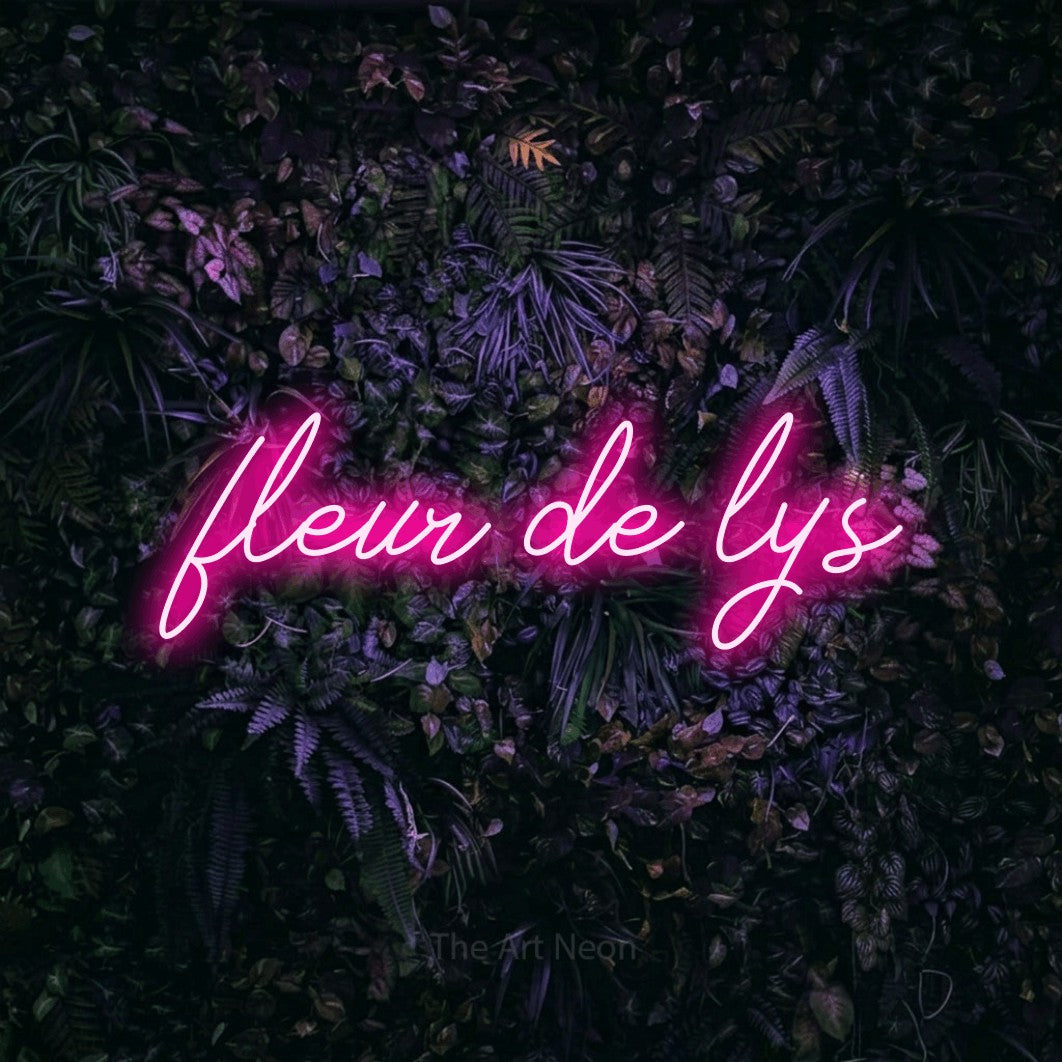 “Fleur de lys” LED neon sign in hot pink, with cursive lettering, shown against a dark wall with purple flowers.