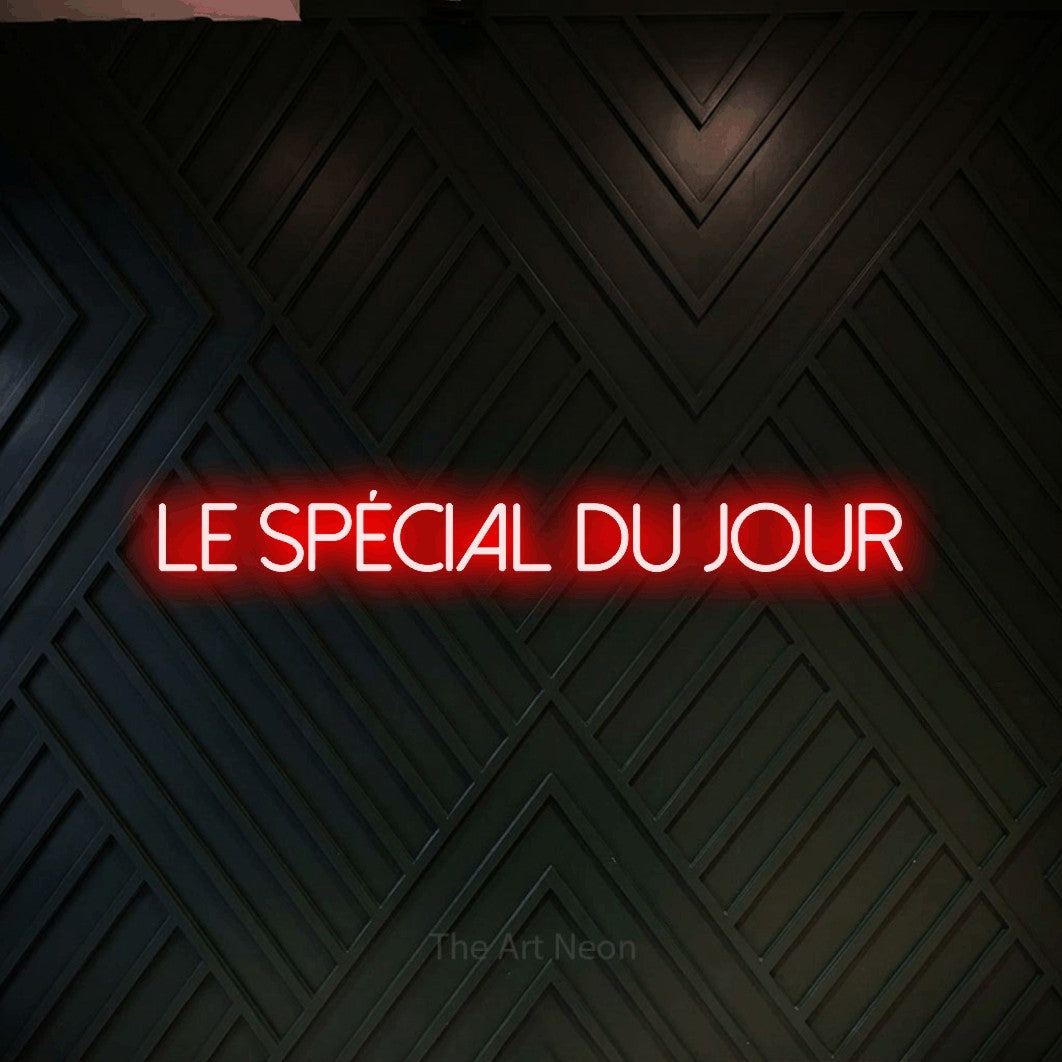 “Le spécial du jour” LED neon sign in red, with thin sans-serif lettering, shown against a black chevron-patterned wood wall.