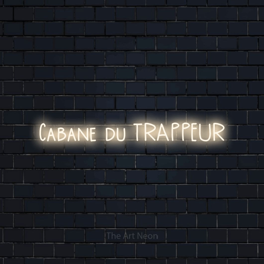 “Cabane du trappeur” LED neon sign in warm white, with narrow hand-drawn lettering, shown against a dark navy brick wall.