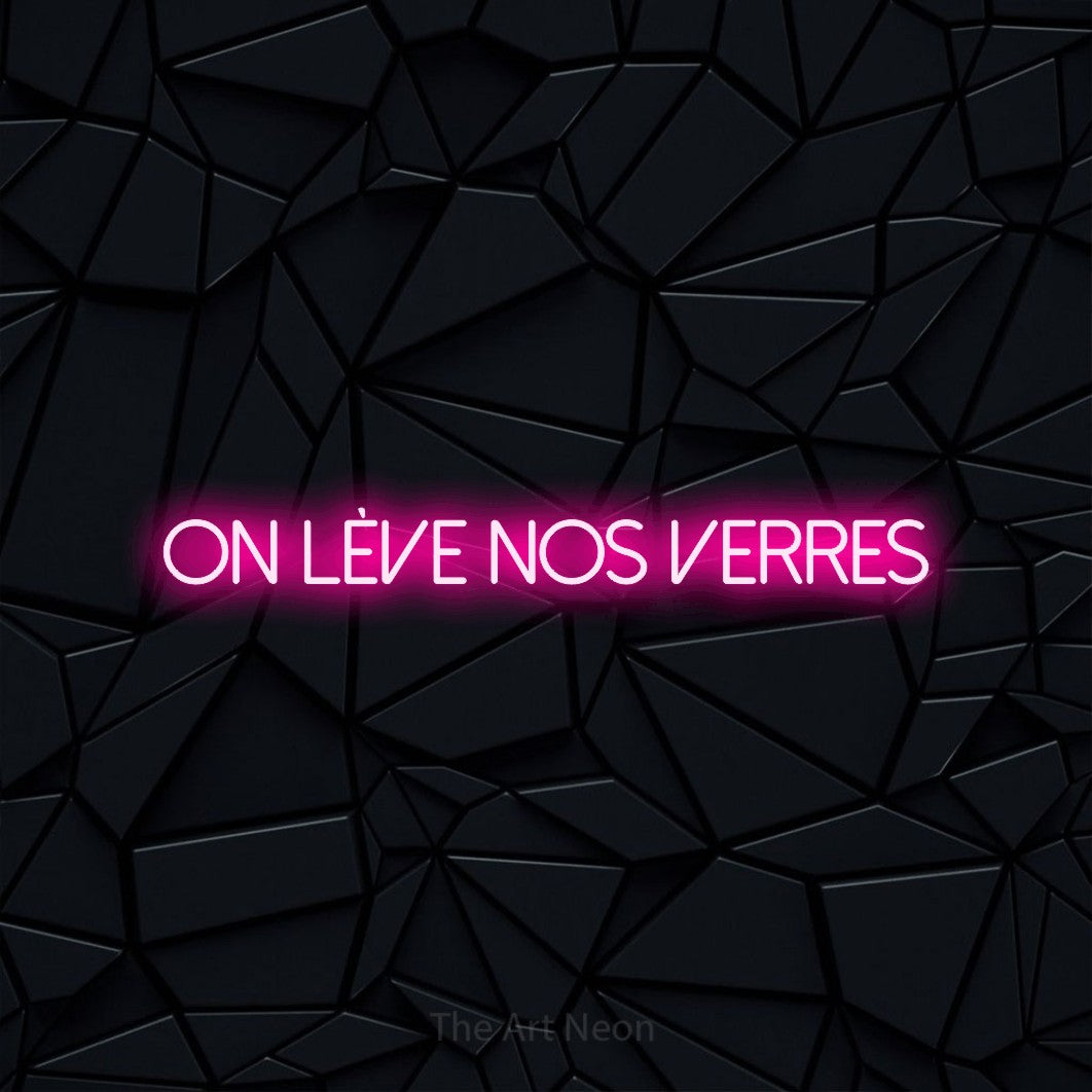 “On lève nos verres” LED neon sign in hot pink, with thin sans-serif lettering, shown against a black polygonal surface.
