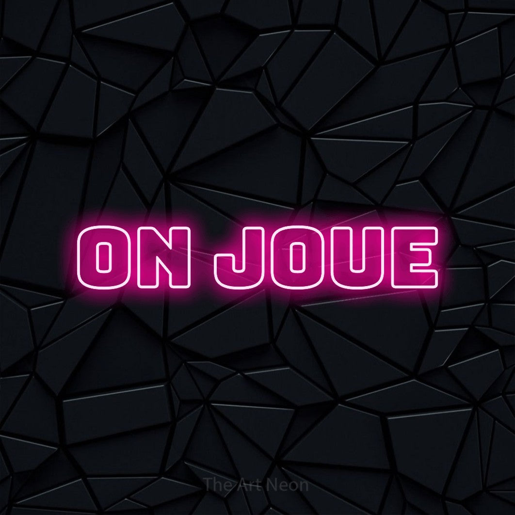 “On joue” LED neon sign in hot pink, with bold outline lettering, shown against a black polygonal surface.