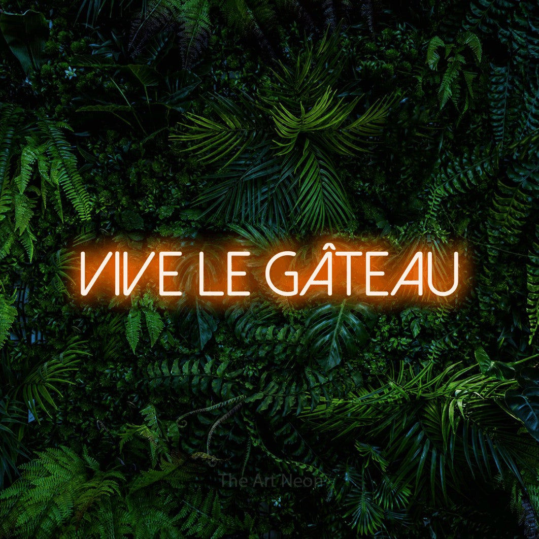 Néon LED « Vive le gâteau » en orange, en lettres fines sans empattement, mis en scène devant un feuillage tropical dense, pour une cuisine.
