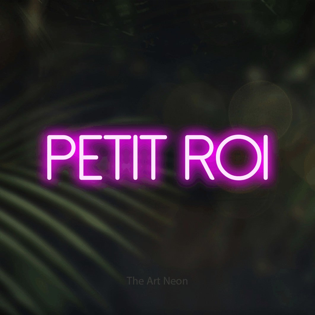 Lettrage en néon LED « Petit roi » en rose, en lettres fines sans empattement, présenté sur un fond flou de palmiers et de lumières bokeh, pour une chambre d’enfant.