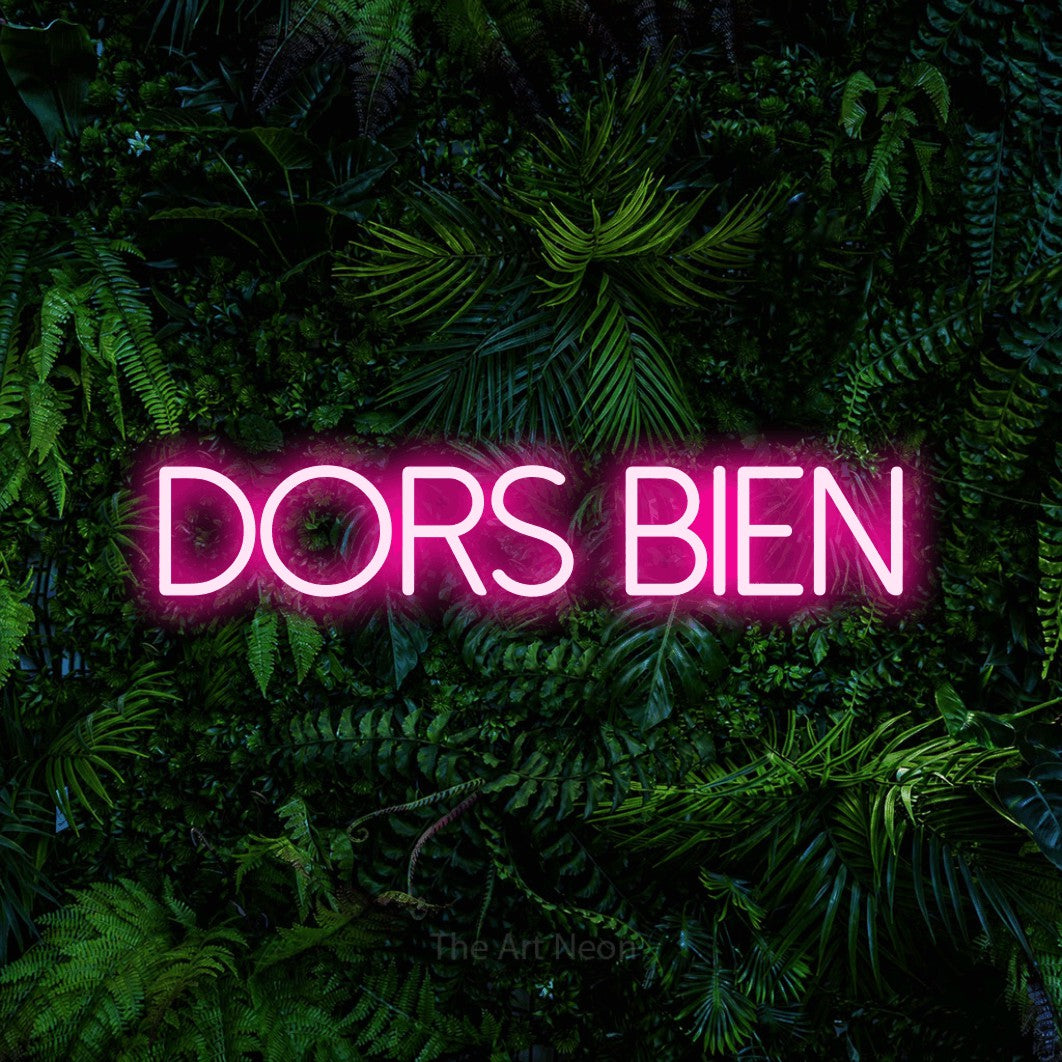 “Dors bien” LED neon sign in hot pink, with thin sans-serif lettering, shown against dense tropical foliage.
