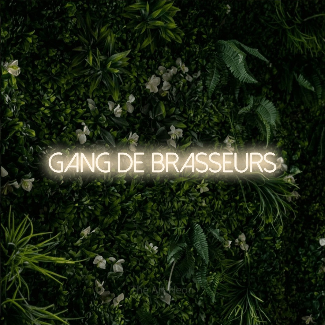 “Gang de brasseurs” LED neon sign in warm white, with thin sans-serif lettering, shown against a dense green plant wall.