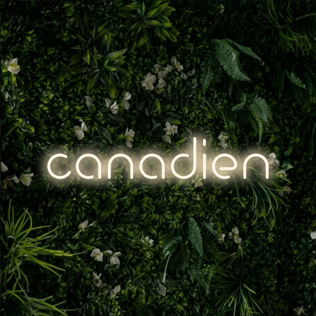 “Canadien” LED neon sign in warm white, with stylised geometric lettering, shown against a dense green plant wall.