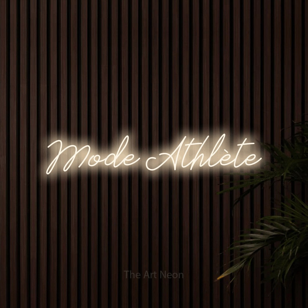 “Mode athlète” LED neon sign in warm white, with cursive lettering, shown against dark wooden wall slats.