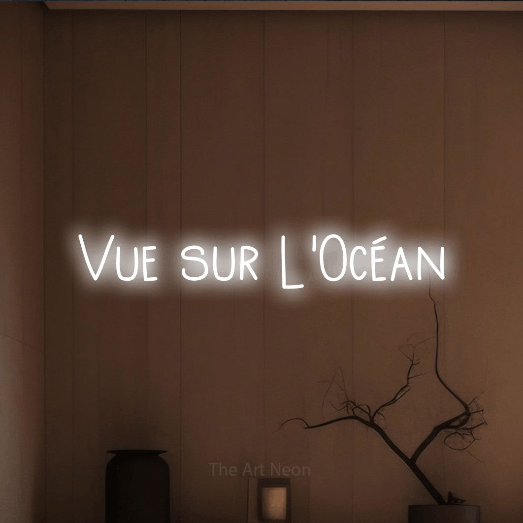 “Vue sur l'océan” LED neon sign in cool white, with narrow hand-drawn lettering, shown against a simple earth-toned interior.