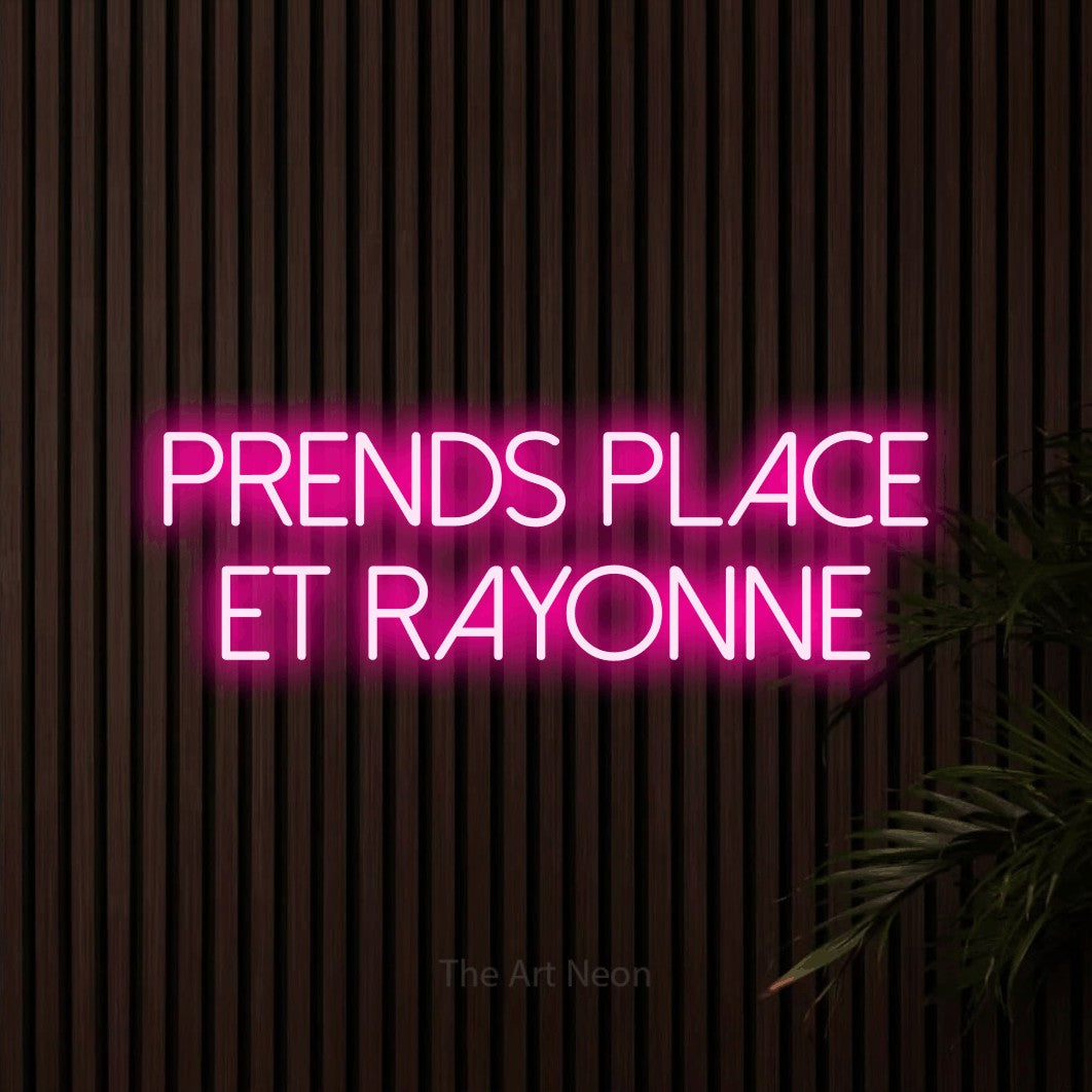 “Prends place et rayonne” LED neon sign in hot pink, with thin sans-serif lettering across 2 lines, shown against dark wooden wall slats.