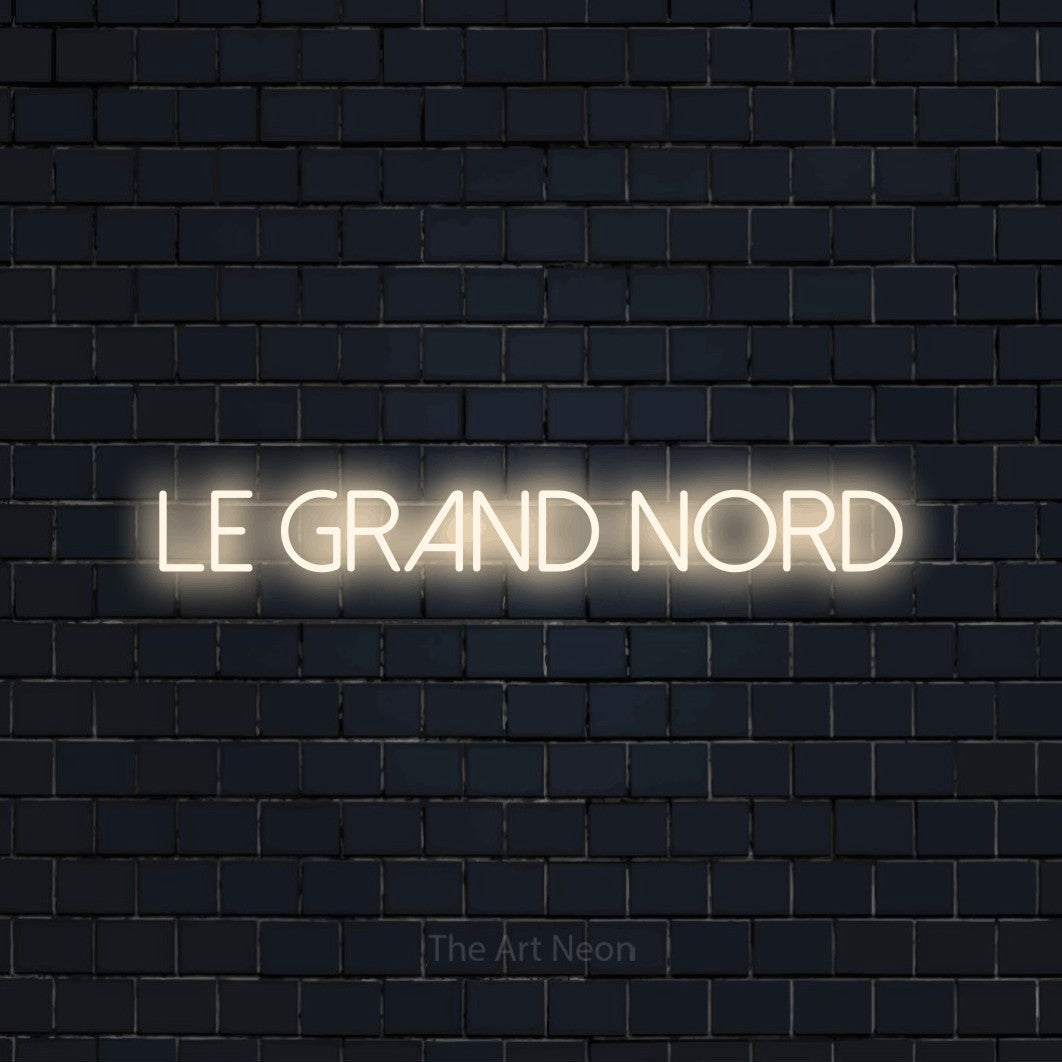 “Le grand nord” LED neon sign in warm white, with thin sans-serif lettering, shown against a dark navy brick wall.