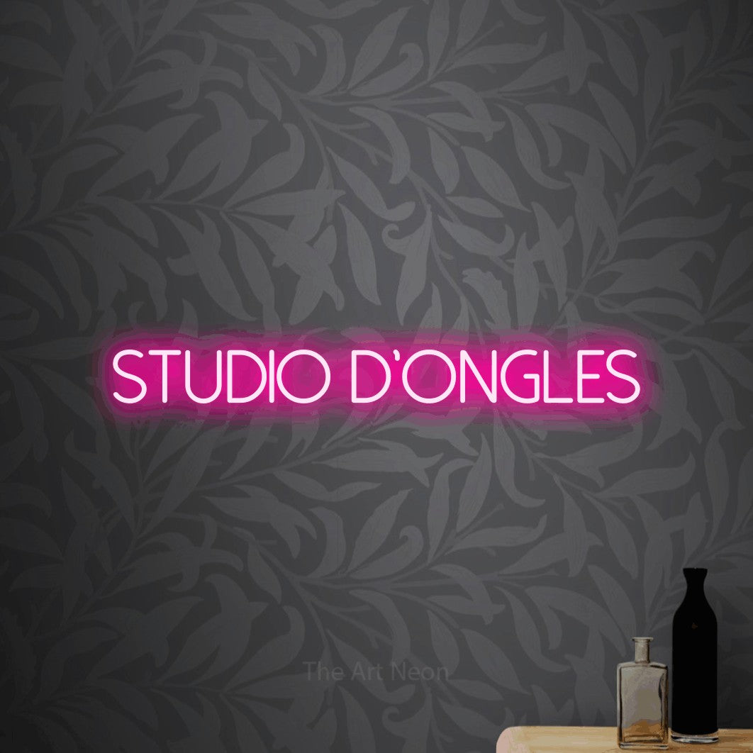 “Studio d'ongles” LED neon sign in hot pink, with thin sans-serif lettering, shown against grey botanical wallpaper.