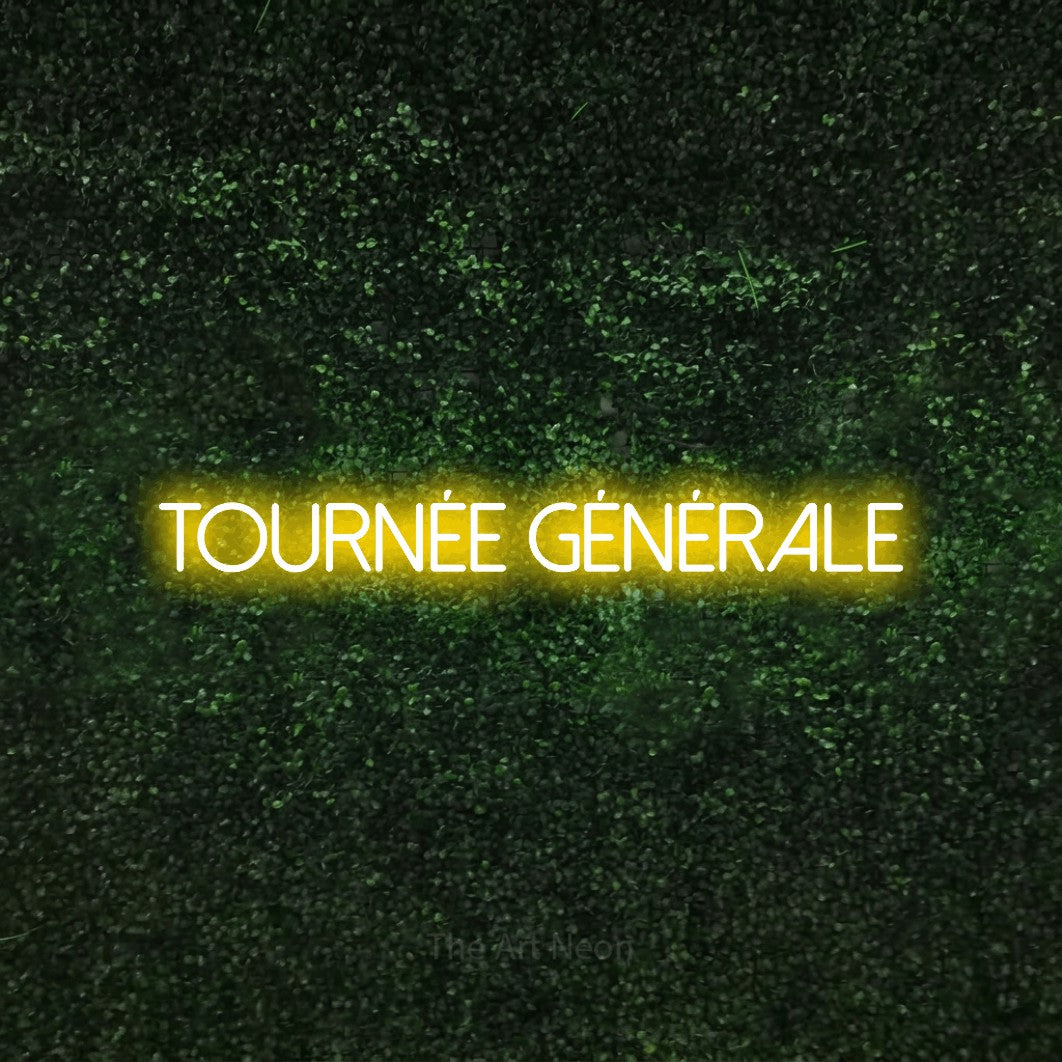 “Tournée générale” LED neon sign in yellow, with thin sans-serif lettering, shown against a textured green hedge.