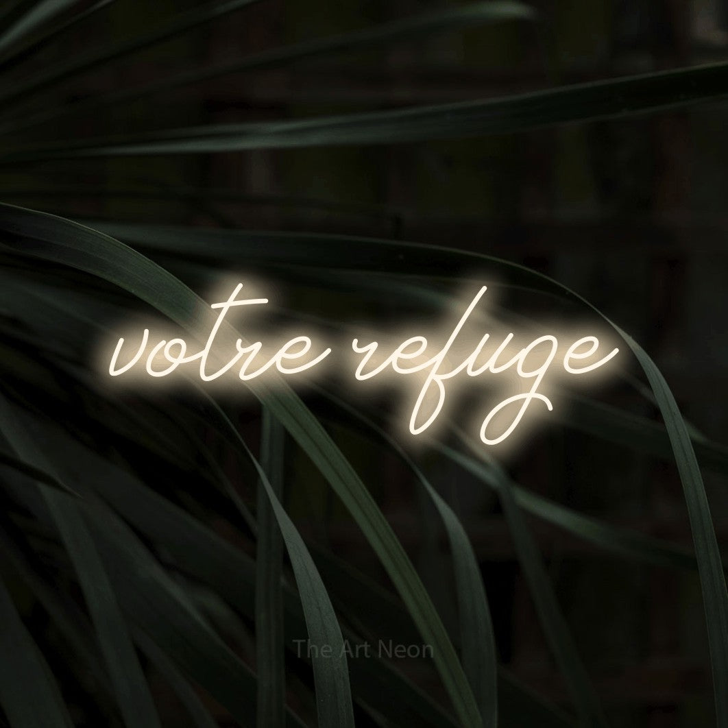 “Votre refuge” LED neon sign in warm white, with cursive lettering, shown against a close-up of dark foliage.