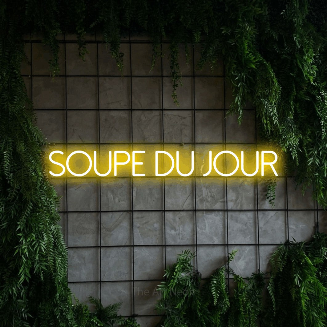 “Soupe du jour” LED neon sign in yellow, with thin sans-serif lettering, shown against an ivy-covered concrete grid.