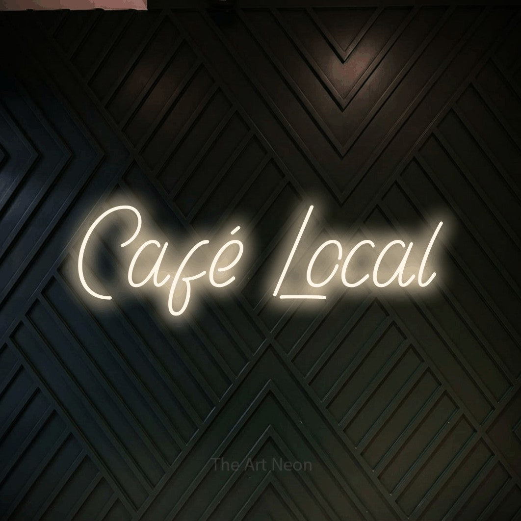 “Café local” LED neon sign in warm white, with slanted handwritten lettering, shown against a black chevron-patterned wood wall.