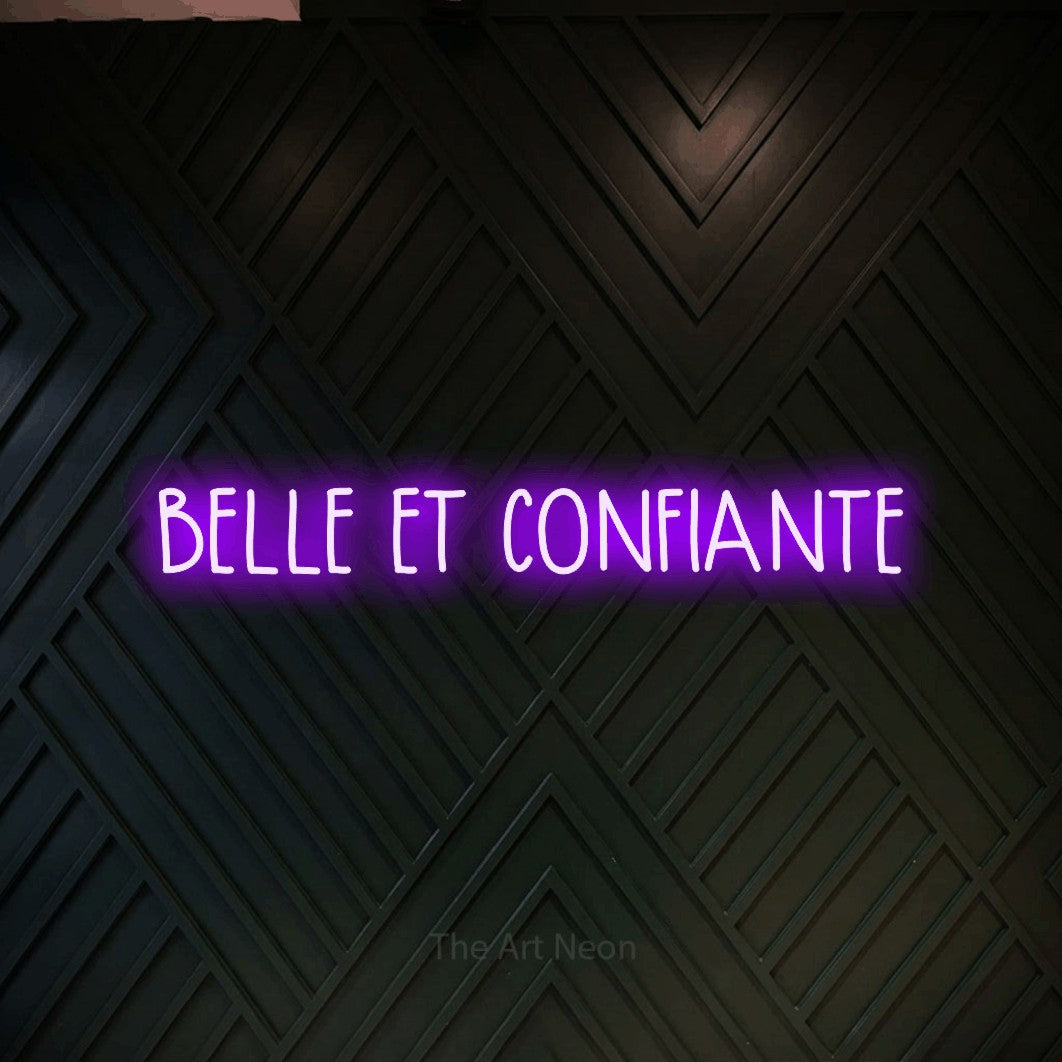 “Belle et confiante” LED neon sign in purple, with narrow hand-drawn lettering, shown against a black chevron-patterned wood wall.