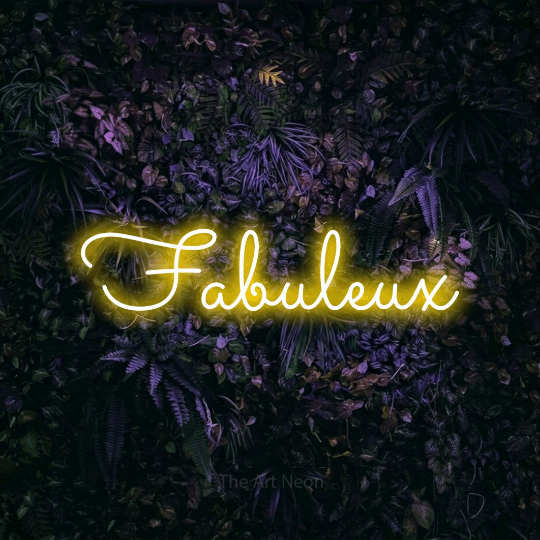“Fabuleux” LED neon sign in yellow, with looped cursive lettering, shown against a dark wall with purple flowers.
