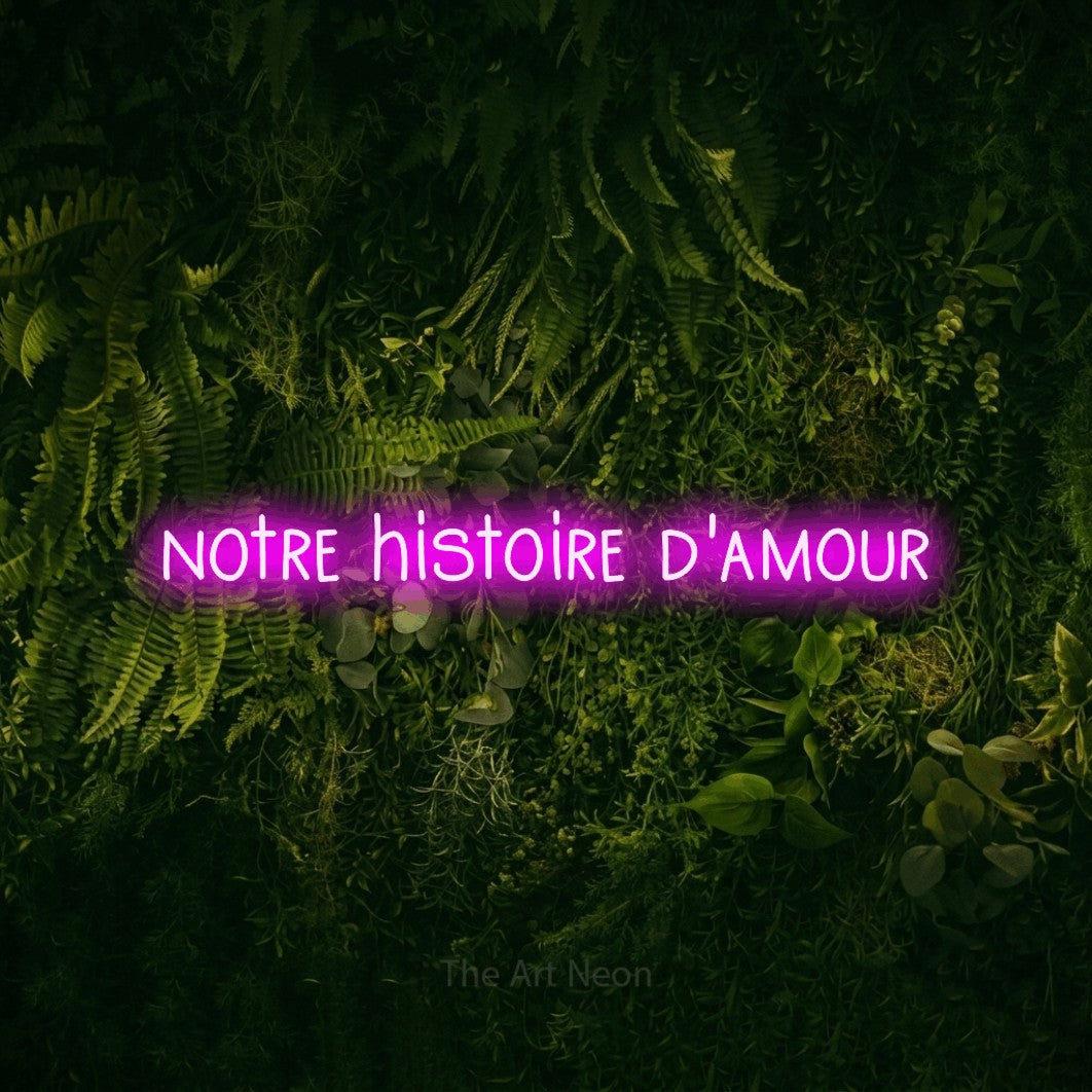 “Notre histoire d'amour” LED neon sign in pink, with narrow hand-drawn lettering, shown against a dark moss and forest backdrop.