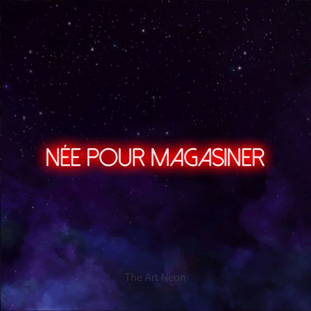 “Née pour magasiner” LED neon sign in red, with thin sans-serif lettering, shown against a purple galaxy backdrop.