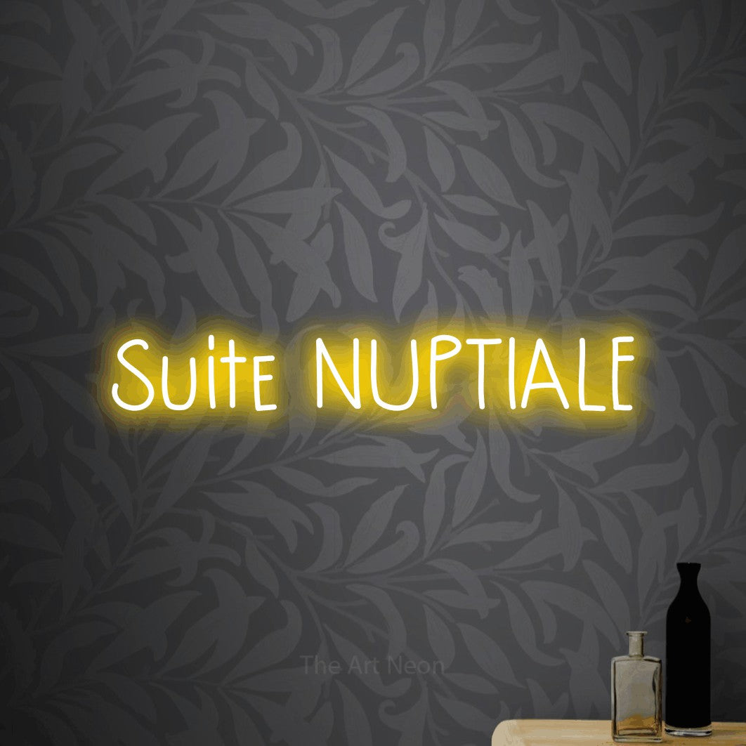 “Suite nuptiale” LED neon sign in yellow, with narrow hand-drawn lettering, shown against grey botanical wallpaper.
