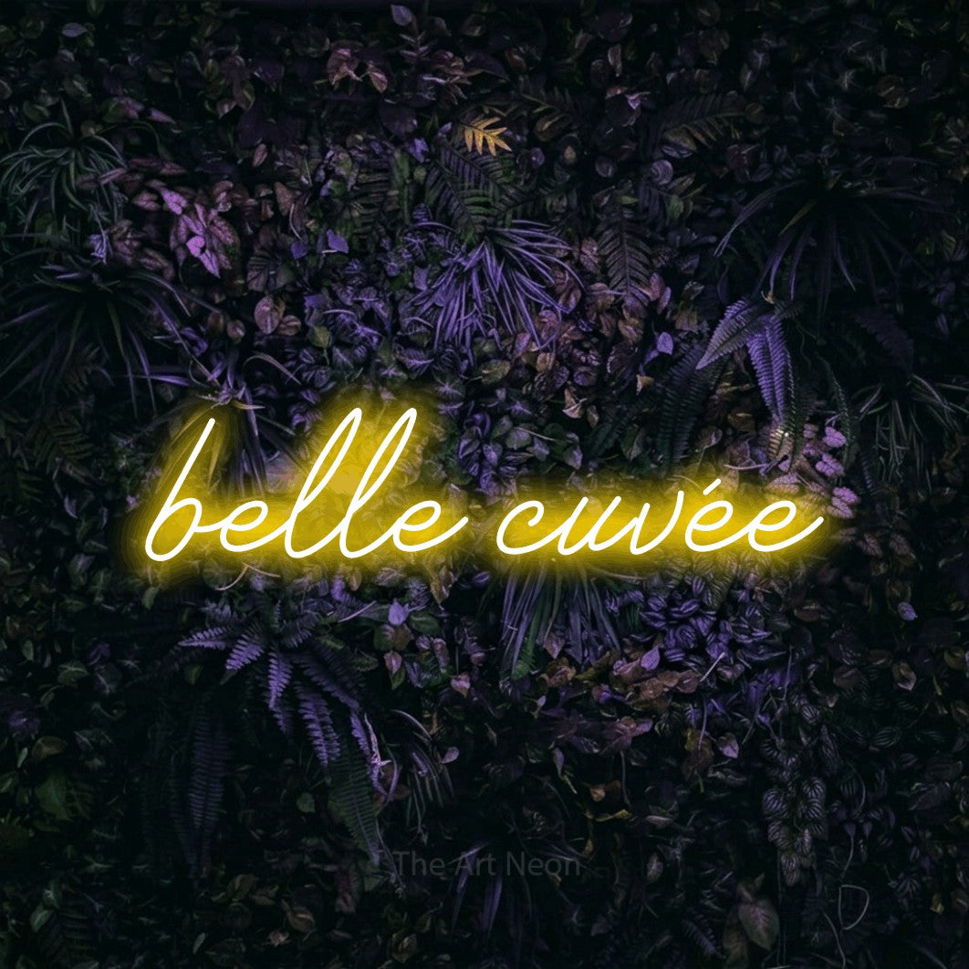 “Belle cuvée” LED neon sign in yellow, with cursive lettering, shown against a dark wall with purple flowers.