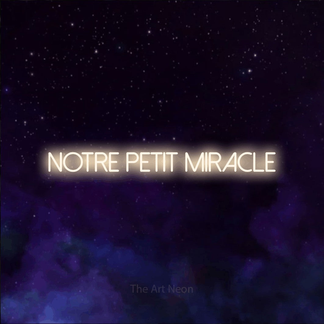 “Notre petit miracle” LED neon sign in warm white, with thin sans-serif lettering, shown against a purple galaxy backdrop.