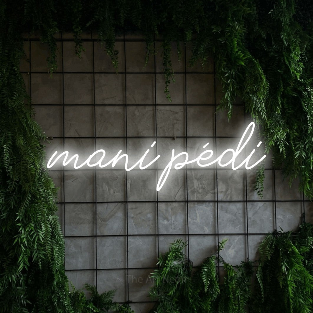Néon LED « Mani pédi » en blanc froid, en lettrage cursif, mis en scène sur une grille de béton couverte de lierre, pour un salon de beauté.