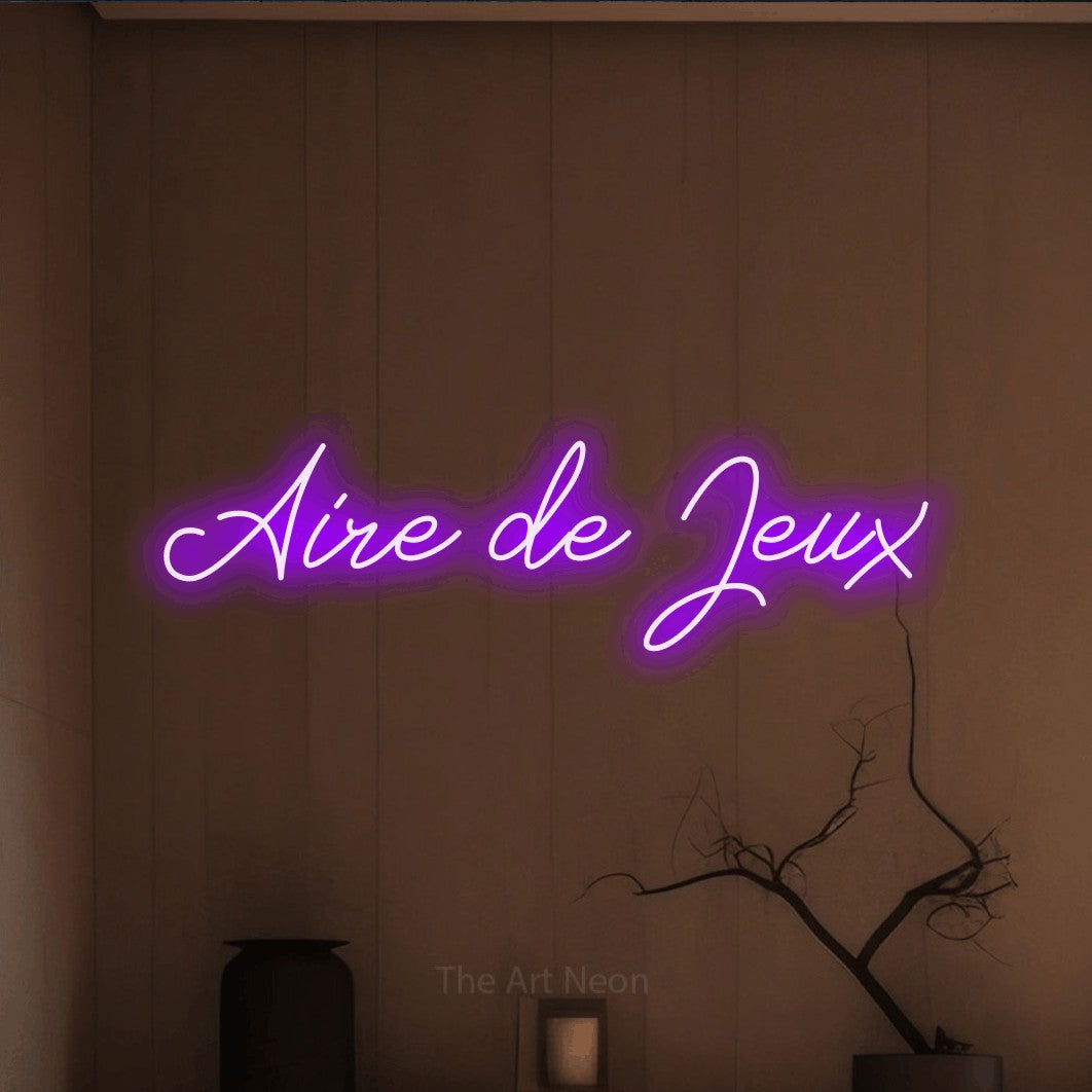 “Aire de jeux” LED neon sign in purple, with cursive lettering, shown against a simple earth-toned interior.
