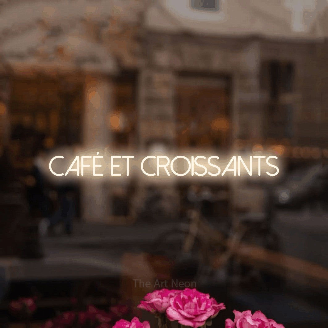 “Café et croissants” LED neon sign in warm white, with thin sans-serif lettering, shown against a blurred café-bar interior.