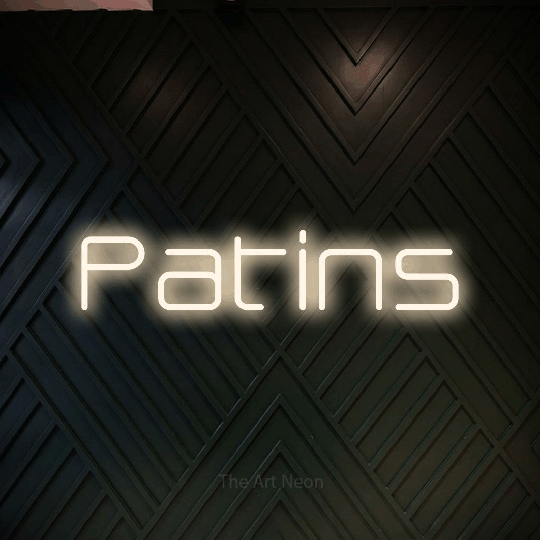“Patins” LED neon sign in warm white, with rounded geometric lettering, shown against a black chevron-patterned wood wall.