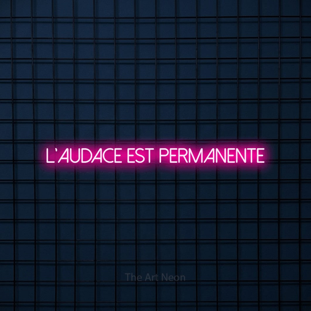 “L'audace est permanente” LED neon sign in hot pink, with thin sans-serif lettering, shown against a dark blue grid.