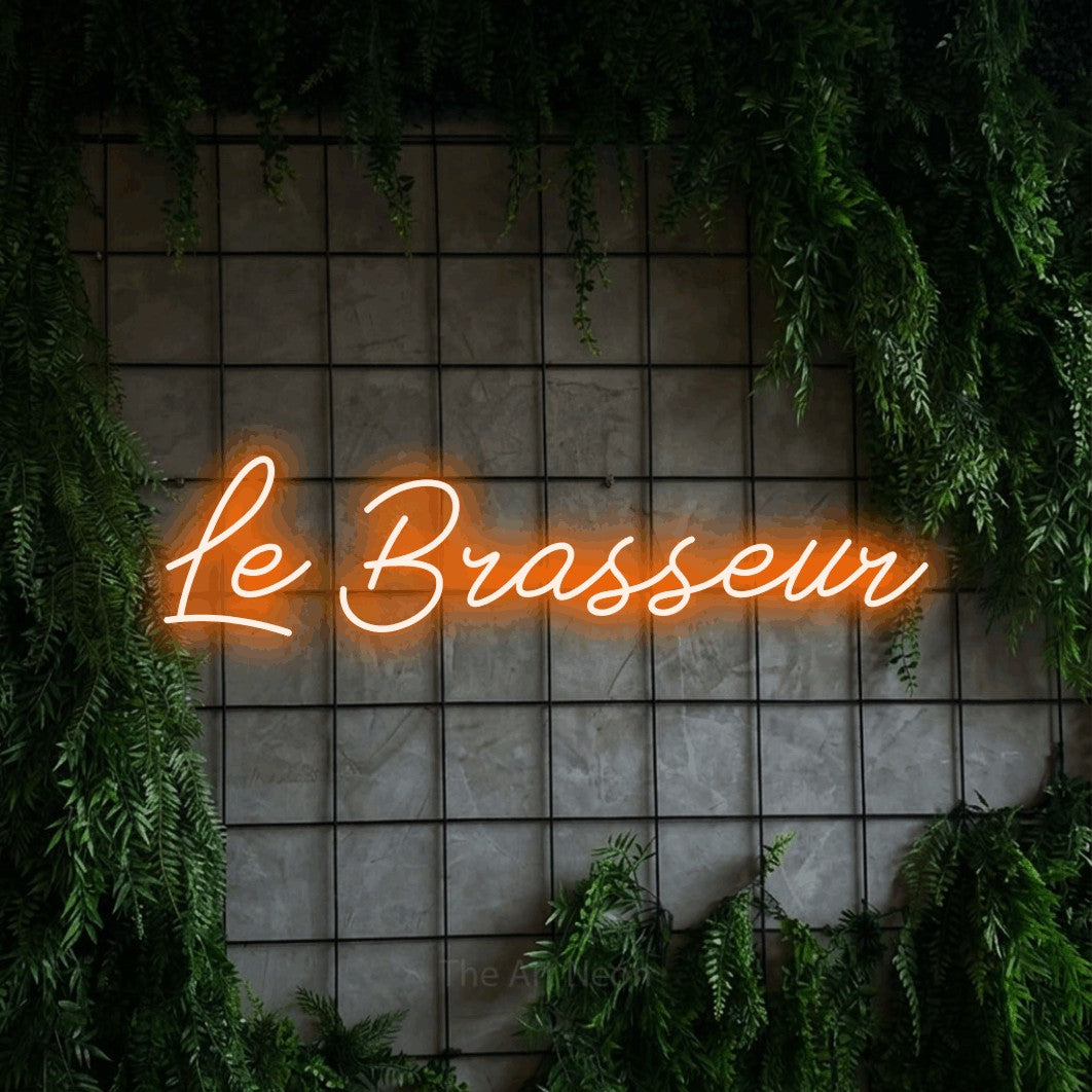 “Le brasseur” LED neon sign in orange, with cursive lettering, shown against an ivy-covered concrete grid.