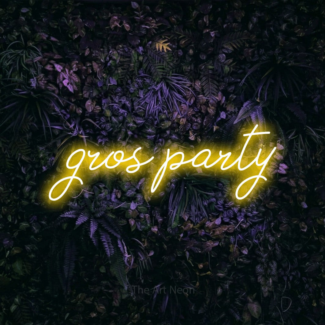 “Gros party” LED neon sign in yellow, with cursive lettering, shown against a dark wall with purple flowers.