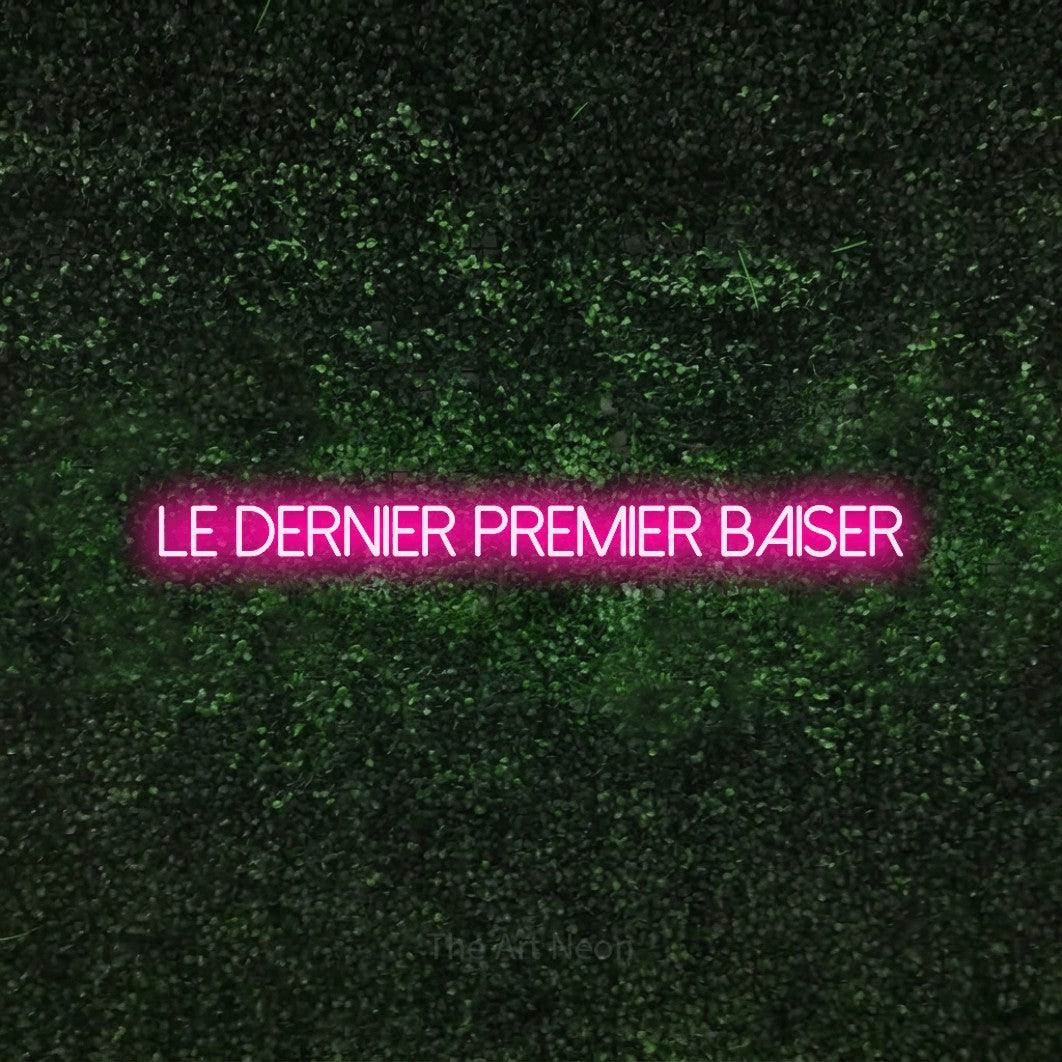 Enseigne néon LED « Le dernier premier baiser » en rose vif, en lettres fines sans empattement, présentée sur une haie verte texturée, pour une réception de mariage.