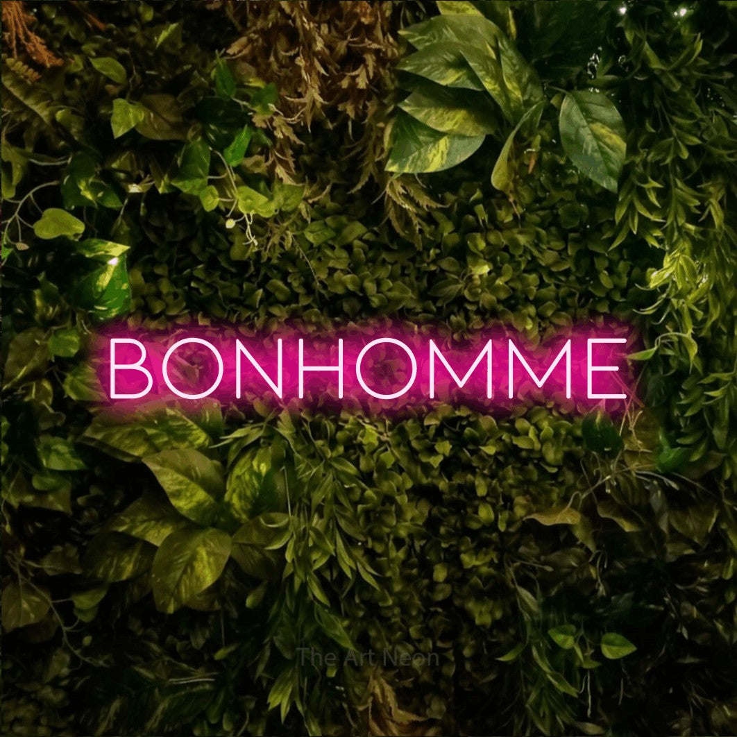 “Bonhomme” LED neon sign in hot pink, with thin, widely spaced lettering, shown against bright green and yellow foliage.
