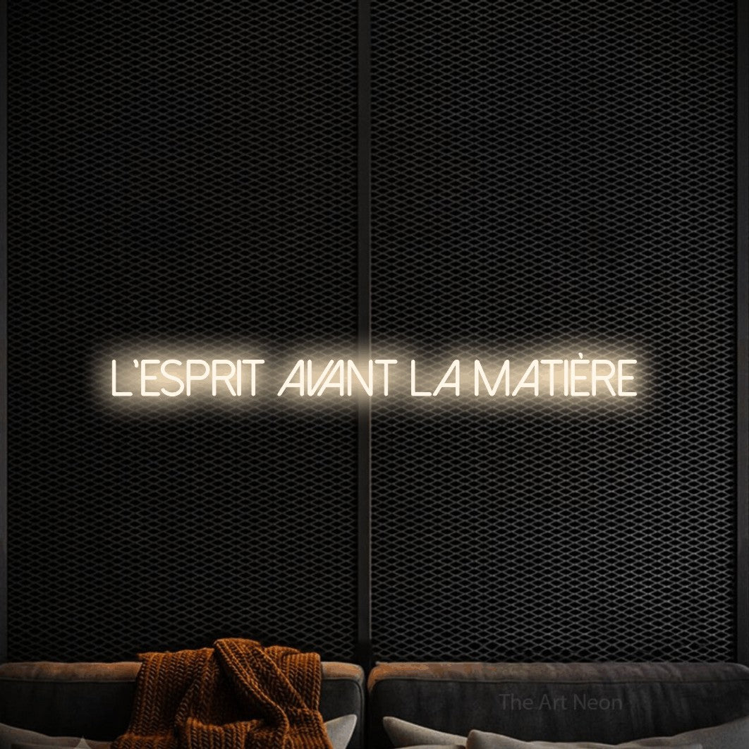 “L'esprit avant la matière” LED neon sign in warm white, with thin sans-serif lettering, shown against a modern dark-toned seating area.