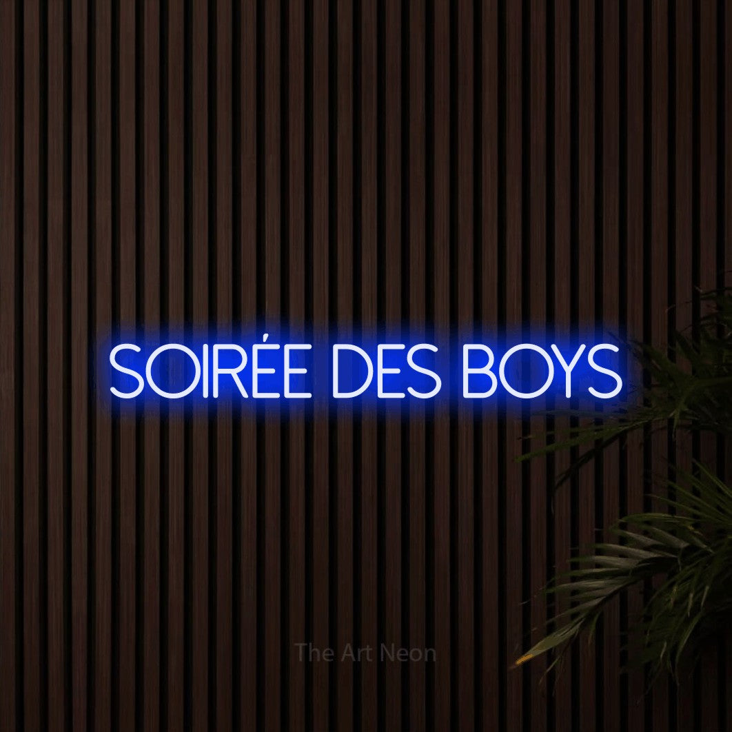 “Soirée des boys” LED neon sign in blue, with thin sans-serif lettering, shown against dark wooden wall slats.